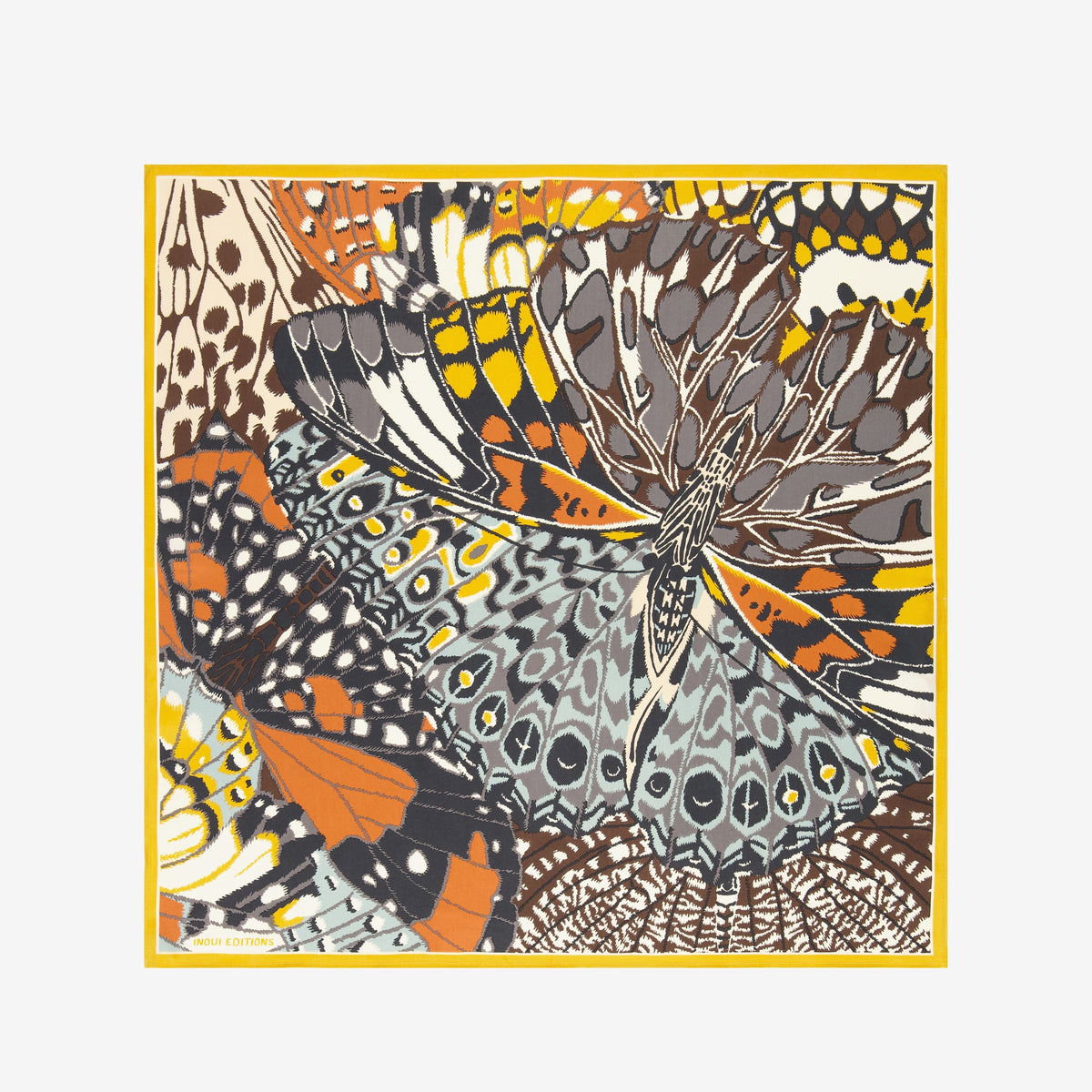 A close-up of a person wearing the INOUI EDITIONS - PAPILLON (BUTTERFLIES) SQUARE WOOL SCARF IN NATURAL by INOUI, draped around their neck over a black top. The scarf showcases abstract and geometric butterfly designs in earthy tones.