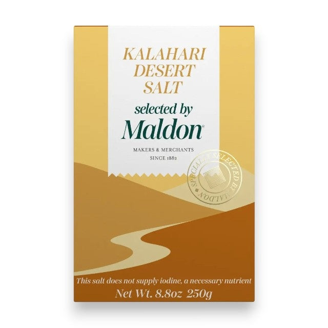 A box of MALDON - KALAHARI DESSERT COARSE SALT by GOURMET FOOD SOLUTIONS. The gold and white packaging features a stylized desert landscape and highlights the product’s essential minerals. This coarse salt delivers the distinct flavor of the arid Kalahari to your table. Net weight: 8.8 oz (250g).