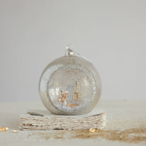 A MERCURY GLASS DIORAMA ORNAMENT WITH DEER, BOTTLE BRUSH TREES AND GLITTER featuring a miniature deer and bottle brush tree inside a mercury glass globe with a snowy diorama.
