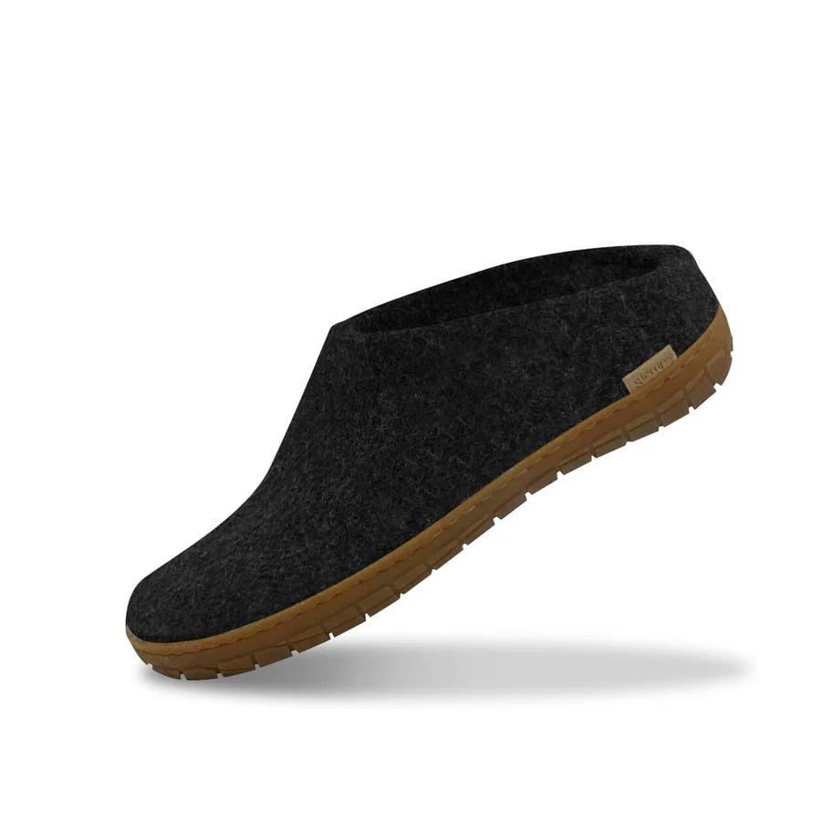 The GLERUPS - SLIP ON SHOE WITH RUBBER SOLE IN CHARCOAL by GLERUPS is a dark gray wool slipper with a natural rubber sole, itch-free slip-on design, and a small tag near the heel, shown in side view on a white background.