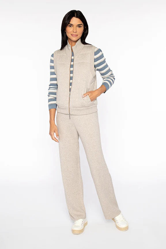 A woman sports the KINROSS CASHMERE - QUILTED ZIP VEST layered over a striped blue and gray long-sleeve cotton shirt, paired with matching gray wide-leg pants and white sneakers, against a plain white backdrop.