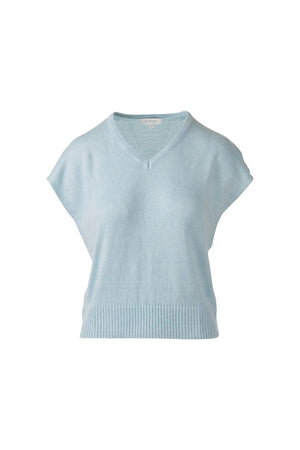 A woman in the KINROSS CASHMERE Cap Sleeve Vee Neck Linen Sweater with blue, brown, and tan stripes and white pants smiles softly against a plain white background.