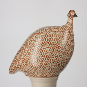 The LES CERAMIQUES DE LUSSAN Medium Ceramic French Guinea in Matte White Spotted Bordeaux is a handmade ceramic sculpture featuring a bird with a rounded body, decorated in a brown and white dotted pattern inspired by French guinea hens, and perched on a simple white cylindrical base.