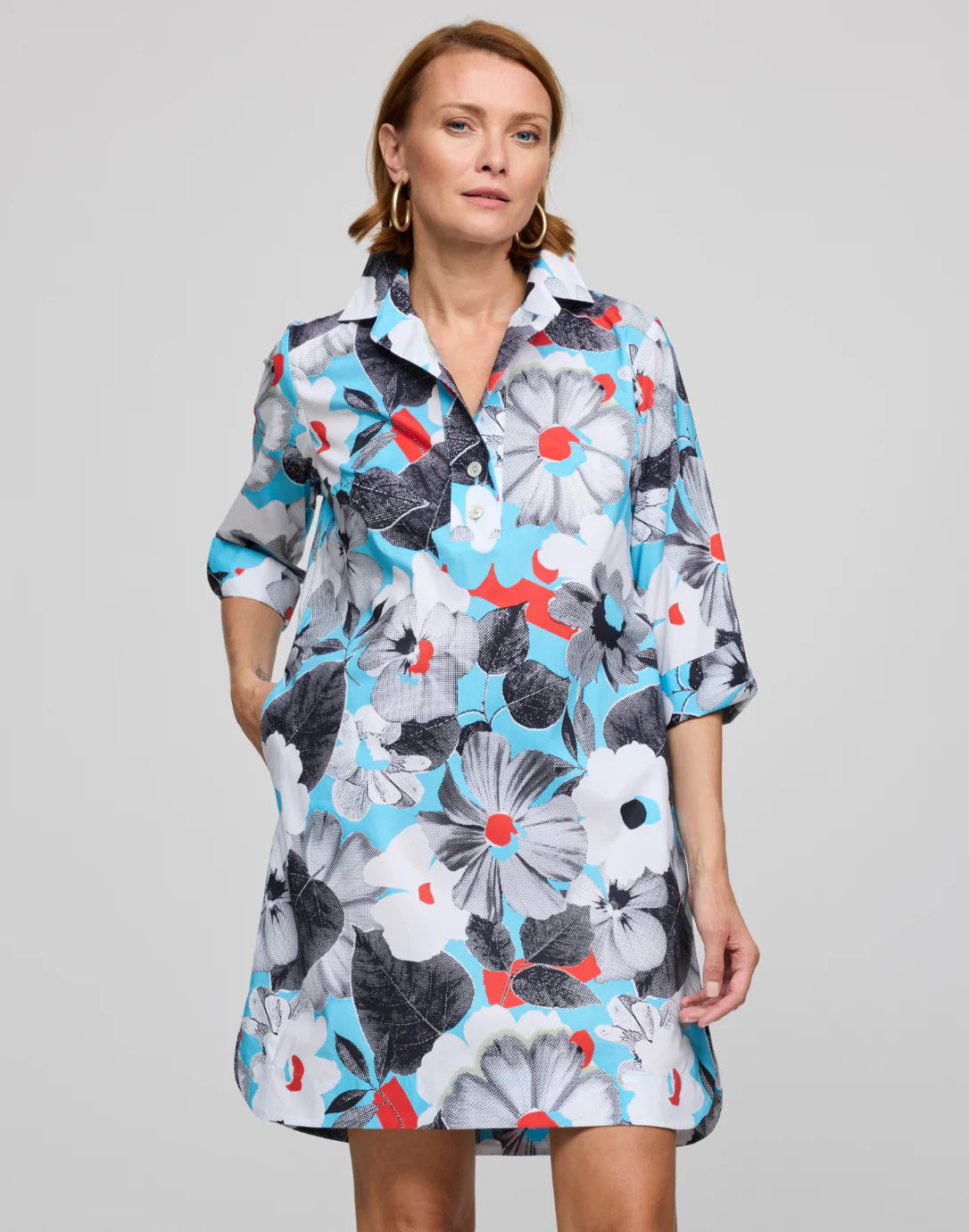 The person is wearing the HINSON WU Aileen dress, featuring a knee-length cut in stretch polished cotton with a pop art flower print in blue, black, white, and red. It has a collared neckline and three-quarter sleeves, stylishly set against a plain gray background.