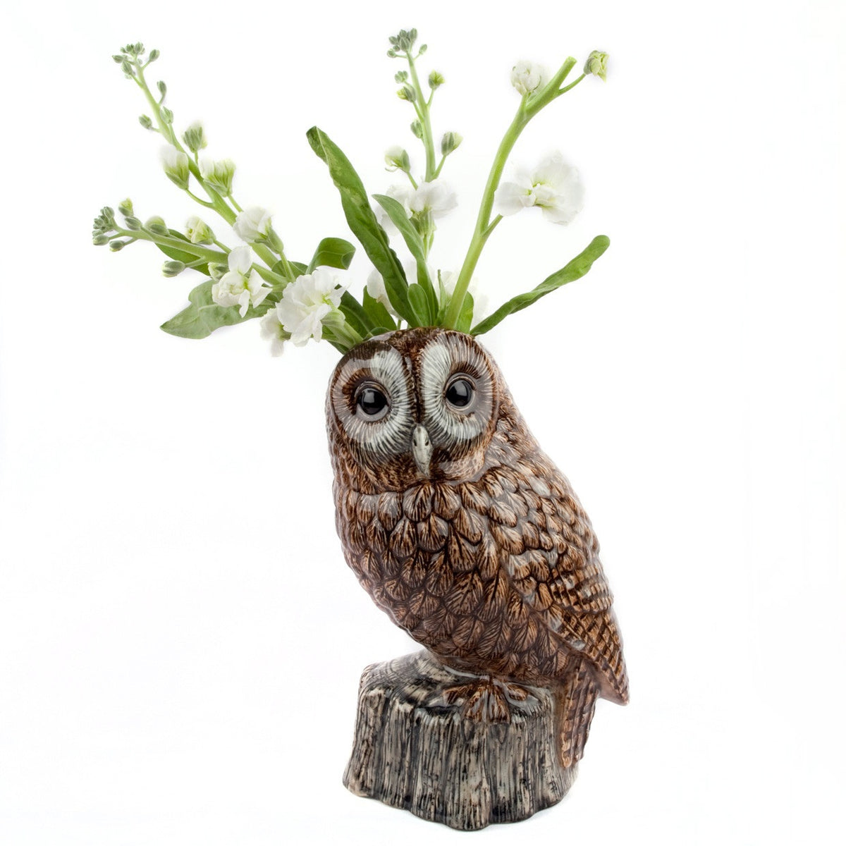 The QUAIL CERAMICS - TAWNY OWL FLOWER VASE by QUAIL DESIGNS features a hand-painted stoneware owl atop a stump-shaped base, with green leaves and white flowers sprouting from its head, set against a plain white background.