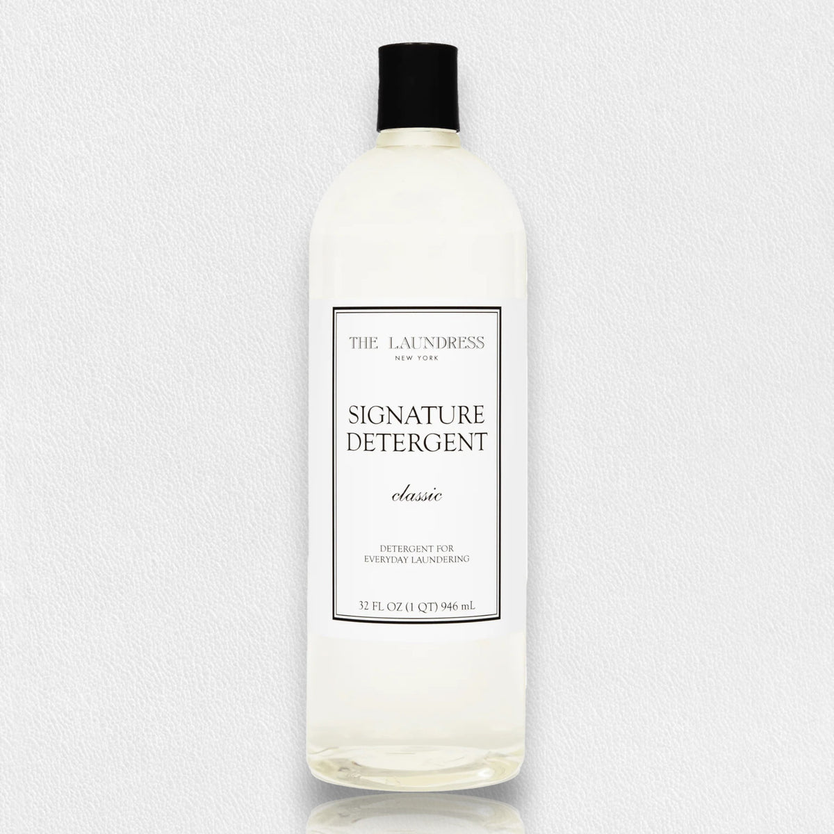 A 32 fl oz (946 ml) bottle of THE LAUNDRESS - SIGNATURE DETERGENT 32OZ featuring a classic scent and bio-based ingredients. The clear bottle comes with a black screw-top lid and a white label showcasing the product name and brand in black text. The background is a simple light gray.