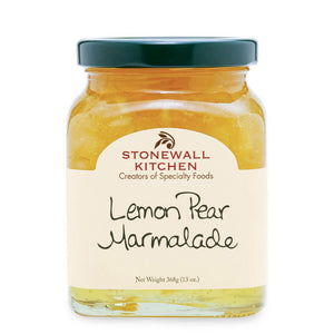A plate featuring two crab cakes garnished with a lemon wedge is served alongside sauce, a jar of STONEWALL KITCHEN Lemon Pear Marmalade, eggs, lobster, chopped peppers, and a fork and napkin on a white table.