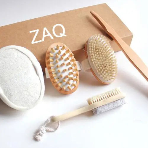 The SHOWER &amp; BATH SET - ZAQ SKIN + BODY CARE by ZAQ SKIN &amp; BODY CARE is a collection of self-care tools that includes an oval pumice stone brush, an oval brush with plastic bristles, a natural shower brush with natural bristles, a long wooden stick, and a small brush with a rope loop. This eco-friendly bath set is displayed near a brown box labeled "ZAQ.