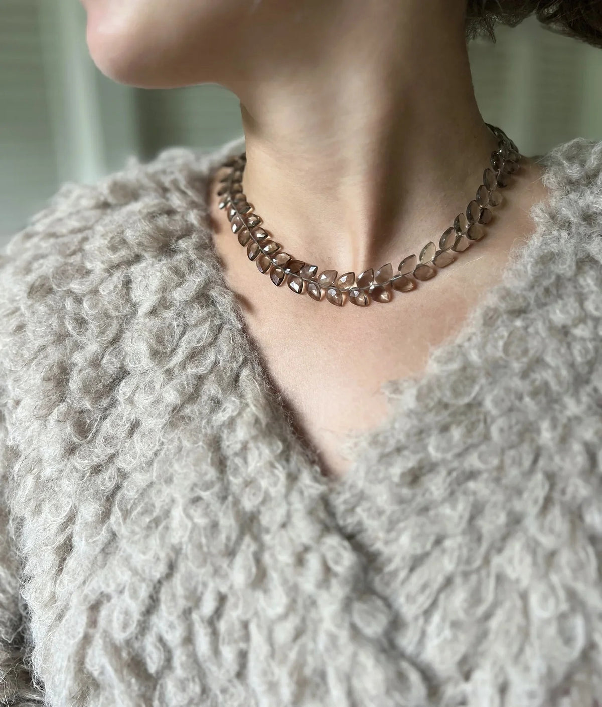 The ANN LIGHTFOOT Faceted Flat Herringbone Cut Smokey Quartz Necklace features leaf-shaped segments linked in a circular pattern, shown on a plain white background.
