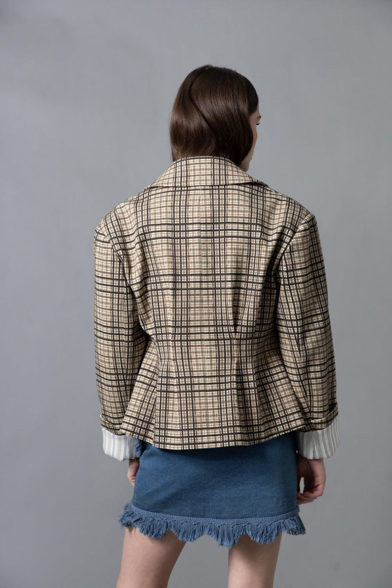 A woman stands sideways against a gray background, wearing the HOPE FOR FLOWERS - FOUR POCKET JACKET by HOPE FOR FLOWERS with a matching beige and brown plaid skirt, white socks, and dark brown heels. Her hair is pulled back as she looks slightly upward.