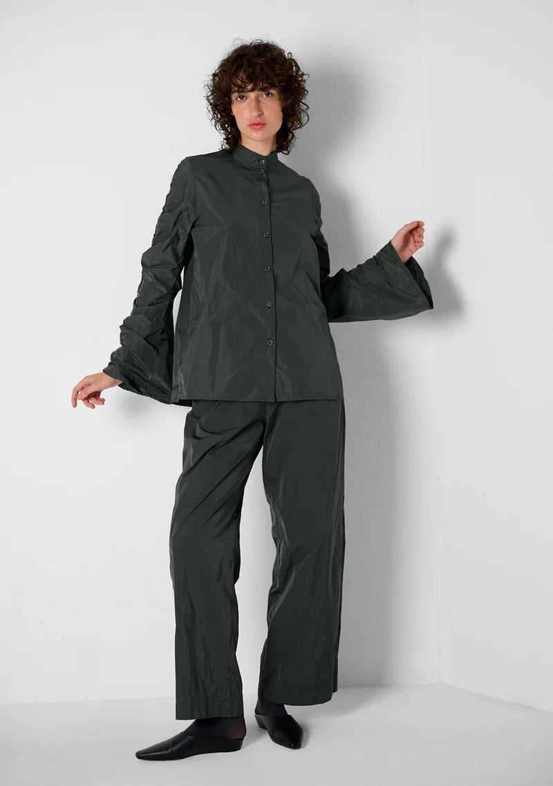 A close-up of KATHARINA HOVMAN&#39;s Easy Pants in anthracite taffeta reveals a textured, possibly dark fabric with a crumpled surface and hints at an elastic waistband due to lighting variations.