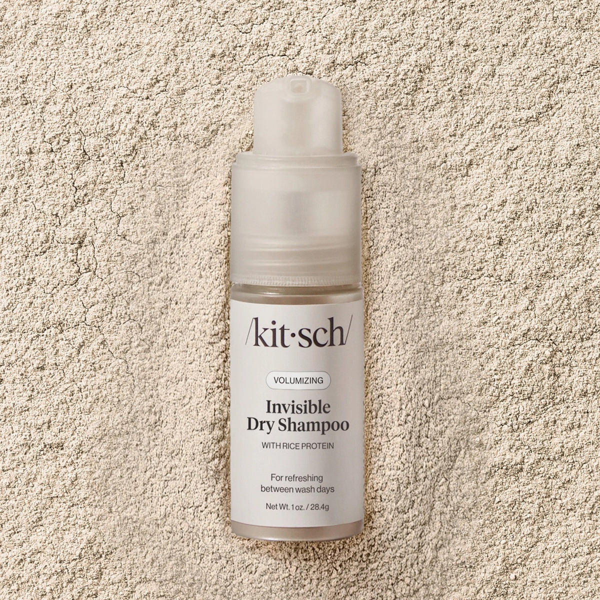 A bottle of KITSCH Volumizing Invisible Rice Protein Dry Shampoo stands upright on a light background. This non-aerosol, mess-free formula by KITSCH refreshes your hair with rice protein and comes with a clear cap and white label.