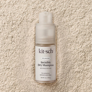 A bottle of KITSCH Volumizing Invisible Rice Protein Dry Shampoo stands upright on a light background. This non-aerosol, mess-free formula by KITSCH refreshes your hair with rice protein and comes with a clear cap and white label.