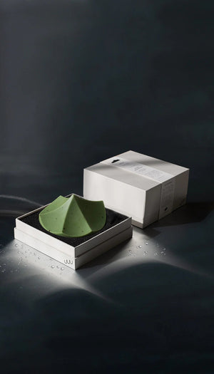 The UME – HERBES DE PROVENCE ERODE SOAP by UME STUDIO is a sculptural, geometric light green bar with subtle speckles and three peaked curves, displayed on a round dark soap dish against a plain white background.