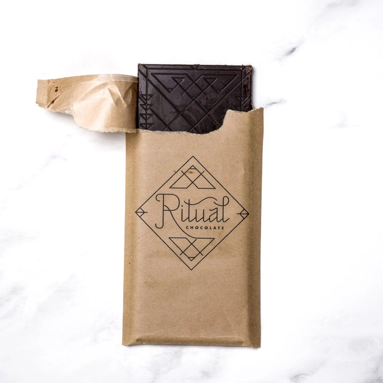 A gold and yellow RITUAL CHOCOLATE - HONEYCOMB TOFFEE CHOCOLATE BAR wrapper with geometric designs holds a 2.12 oz (60 g), 75% cacao single origin dark chocolate bar, displayed on a marble background.