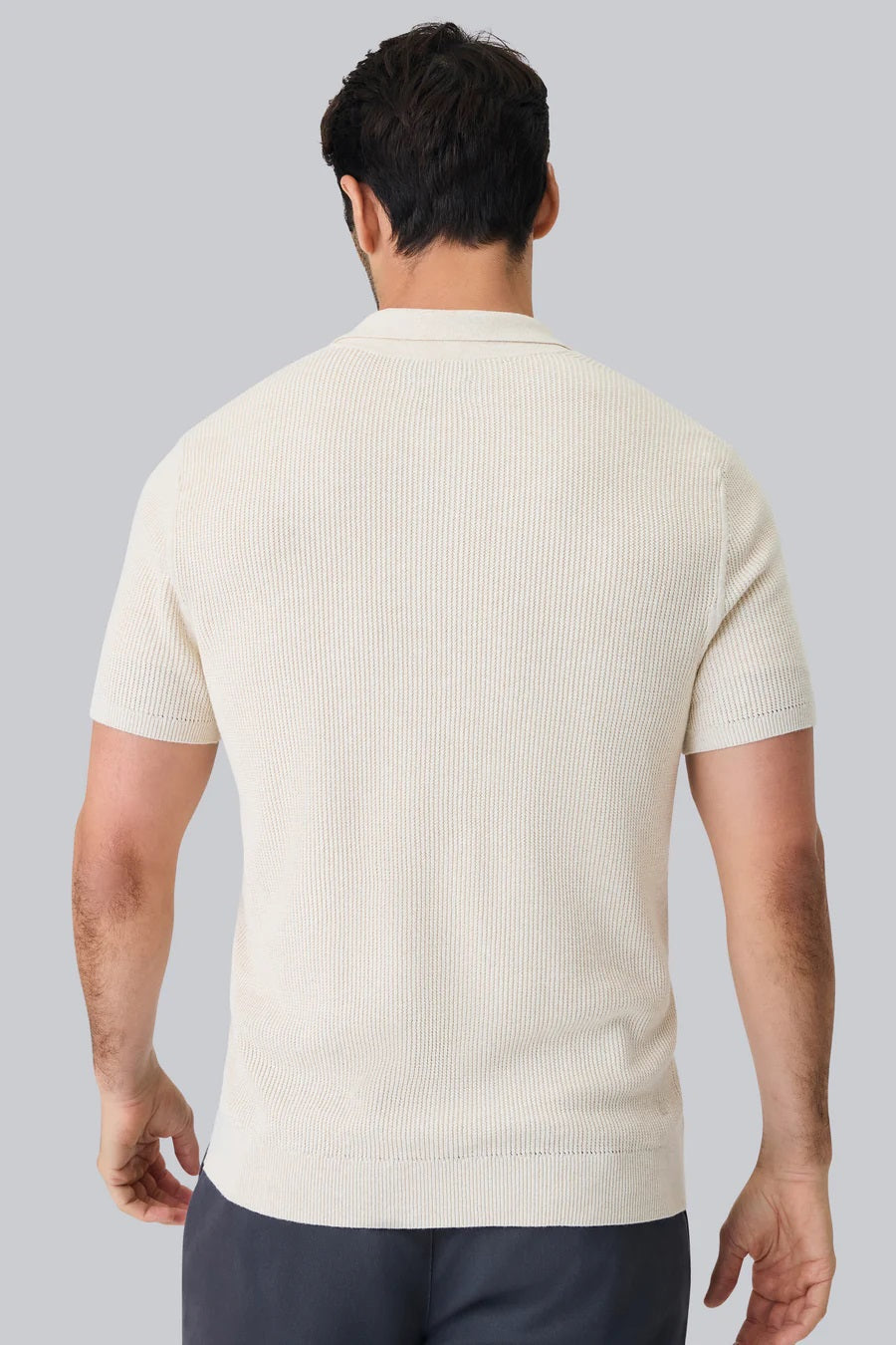 A man with dark hair and a short beard models the MACK WELDON Tech Linen Button Up Sweater Polo in Latte Heather, standing hands-in-pockets against a white background and looking effortlessly stylish and comfortable.