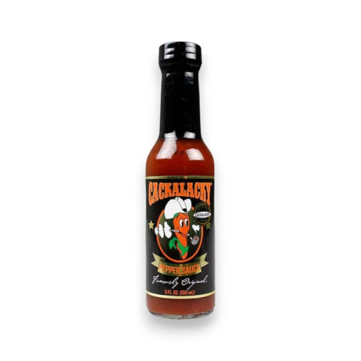 A 5 fl oz (150 ml) bottle of CACKALACKY - JACK PEPPER SAUCE GOLD by CACKALACKY, featuring a black label with a cartoon pepper in a chef’s hat, plus white, orange, and green text. This is an all-natural hot sauce.