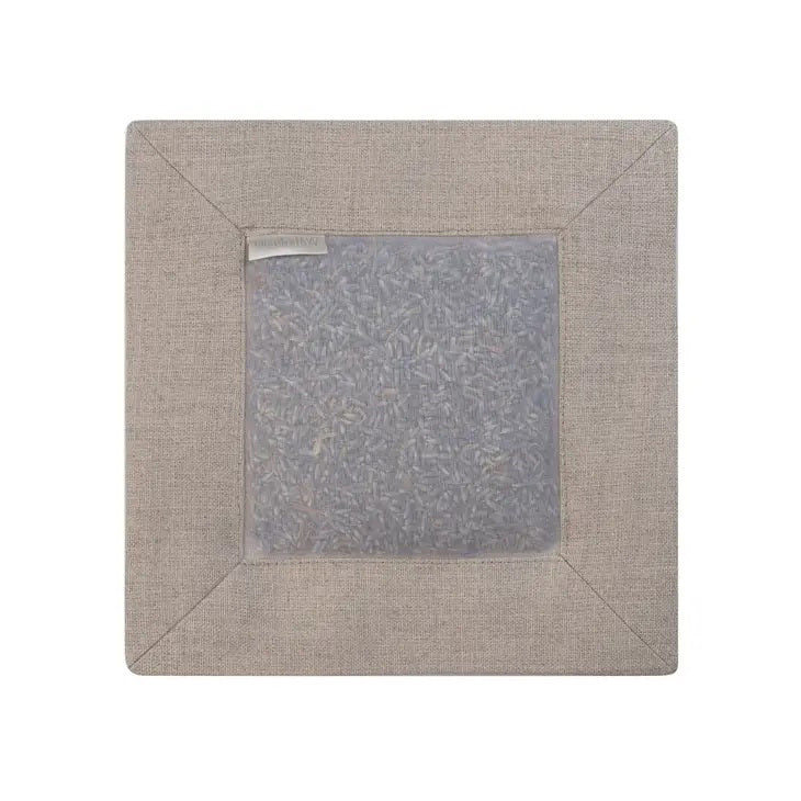 The SQUARE LAVENDER SACHET IN NATURAL LINEN by E WIGHTMAN &amp; CO features a square design with a beige silk and natural linen fabric border. A central translucent window elegantly displays the dried lavender buds inside. This minimalist sachet includes a small label on one side and is showcased against a plain white background.