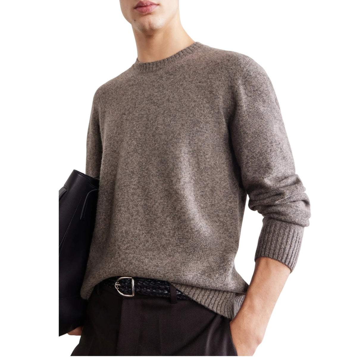 A person wearing the HARTFORD Seamless Wool Crew Pullover in Mushroom, an Italian-made sweater, paired with dark pants, is seated with one arm resting on their knee against a plain light background.