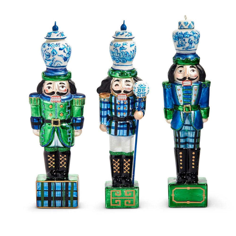 The BLACK WATCH NUTCRACKER ORNAMENT by RAZ IMPORTS features blue and green uniforms and holds a glass vase on its head. Sold individually, each square base displays a unique geometric pattern.