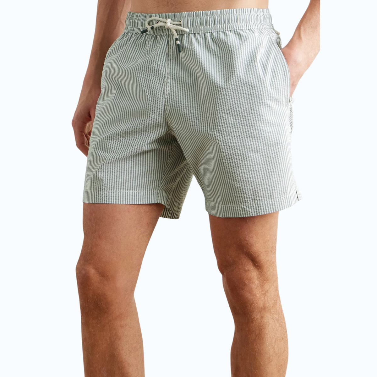 A person wearing HARTFORD - SEERSUCKER SWIM TRUNKS IN GREEN with an elastic waistband and drawstring stands against a plain light background.