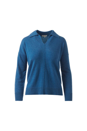 A woman stands against a white background, wearing the KINROSS CASHMERE Splitneck Polo in cashmere. She pairs it with matching pants, poses relaxedly while holding the hem of her top, and smiles softly.