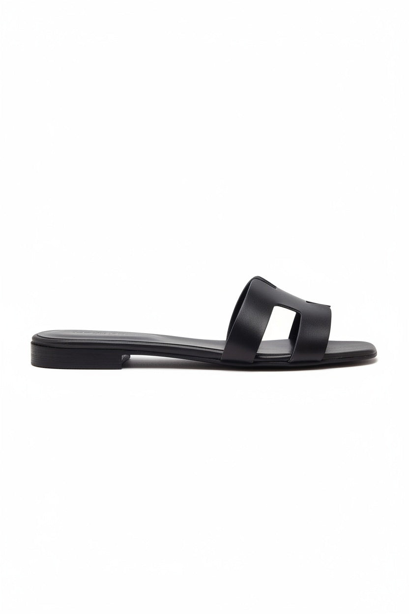 The MICHELE LOPRIORE - H SLIDE is a brown leather sandal with two wide straps, including one with a rectangular cutout, featuring a flat wooden sole. Made in Italy by MICHELE LOPRIORE, it's shown on a white background.