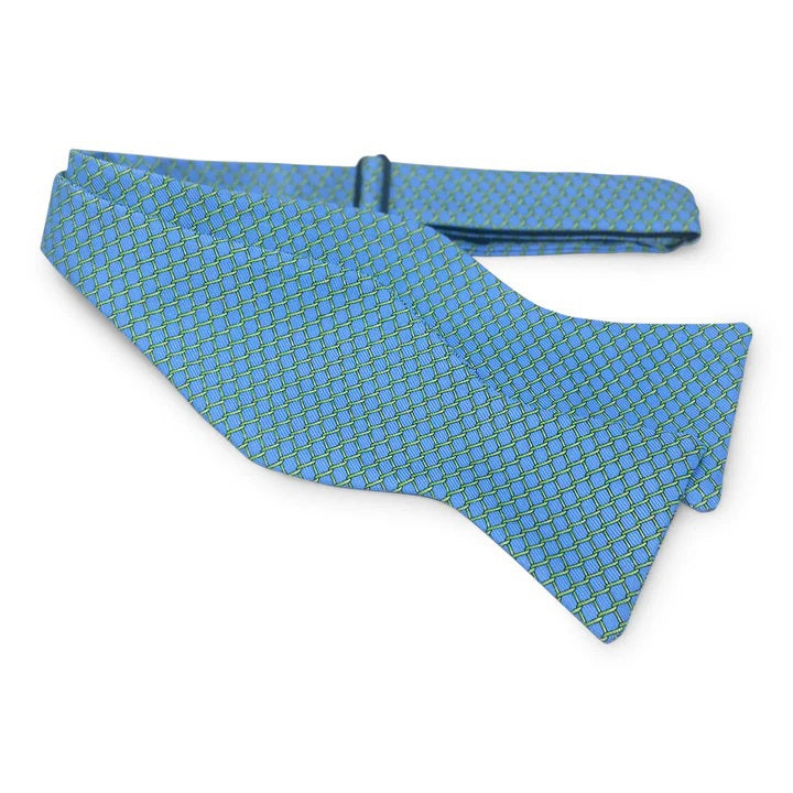 The PETER-BLAIR Fencing Silk Bow Tie in Blue by BIRD DOG BAY is a butterfly-shaped silk tie with a green and light blue geometric grid pattern, adjustable neck sizing, shown on a white background.