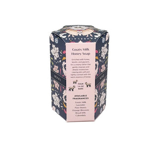 A decorative BAUDELAIRE - GOATS MILK HONEY SOAP 1.4 OZ QUARTET box sits beside a stack of four pale pink, hexagon-shaped soap bars. The floral-patterned box features an illustration of a goat, drawing attention to this gentle triple-milled soap from BAUDELAIRE, crafted with nourishing goat milk and natural honey.