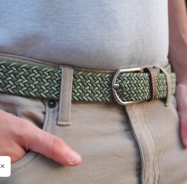 The ROOSTAS - REMINGTON WOVEN STRETCH BELT features a green herringbone weave, brown leather accents with embossed logo, decorative stitching, and a silver buckle. Adjustable for comfort and style on any occasion.