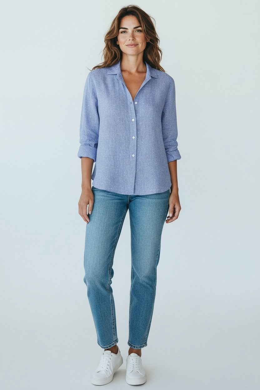A woman faces forward in the FRANK &amp; EILEEN EILEEN Relaxed Button Up in Blue Italian Linen with Hearts, paired with blue jeans and white sneakers, against a plain light background.
