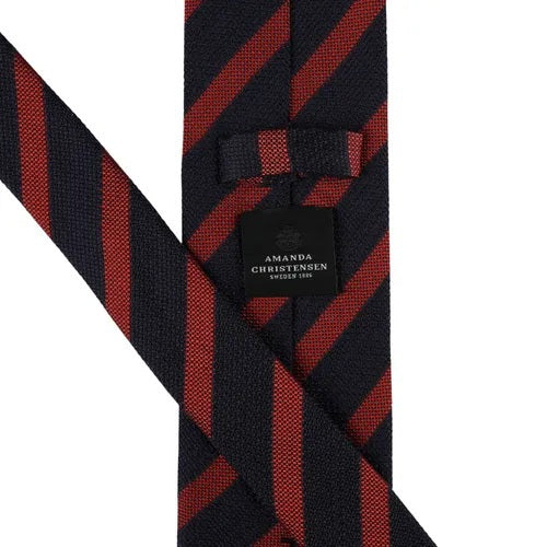 A close-up of the AMANDA CHRISTENSEN - STRIPED JACQUARD WOVEN SILK TIE IN RUST reveals its elegant red diagonal stripes on luxurious Italian silk, with a label bearing the AMANDA CHRISTENSEN name against a white background—an exceptional men’s formal accessory perfect for any refined occasion.