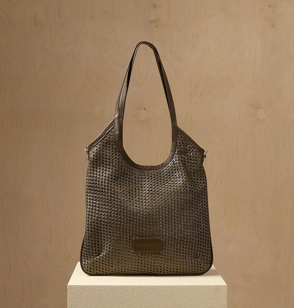 The DANIELA LEHAVI - ALBA HOBA SAC, a tan woven handbag with a single leather crossbody strap from DANIELLA LEHAVI, is displayed on a light pedestal against a beige background.