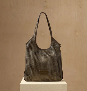 The DANIELA LEHAVI - ALBA HOBA SAC, a tan woven handbag with a single leather crossbody strap from DANIELLA LEHAVI, is displayed on a light pedestal against a beige background.