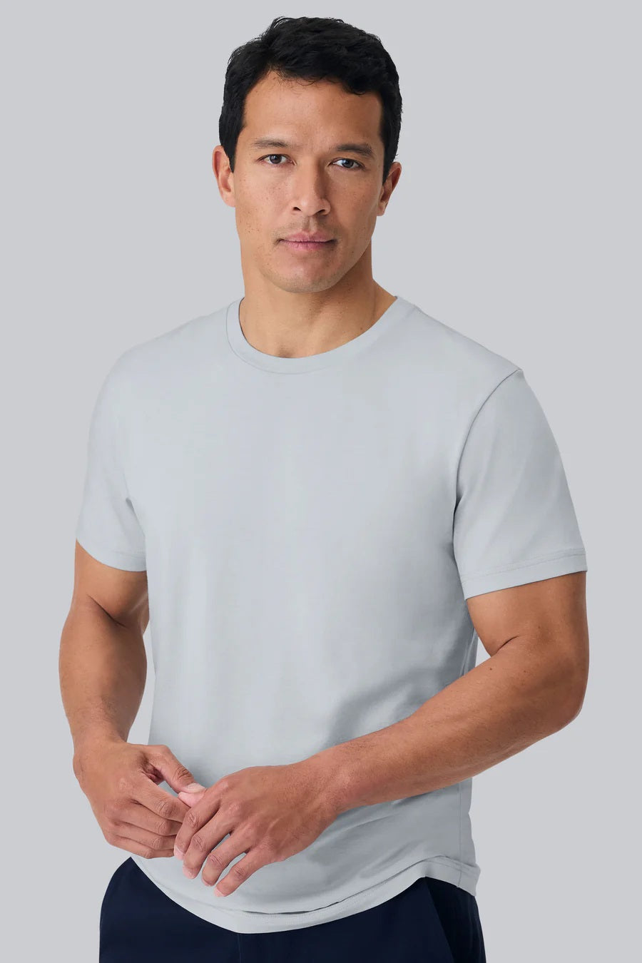 A man with short dark hair wears the MACK WELDON Pima Crew Neck T-Shirt in Steam and dark pants, standing against a plain light gray background and looking at the camera with a neutral expression.