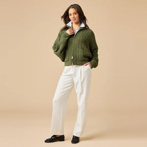 A woman wearing a cream-colored, plush SOFTIES - CABLE KNIT MARSHMALLOW FUNNEL NECK DOUBLE ZIP JACKET with a funnel neck and double zipper, paired with blue jeans.