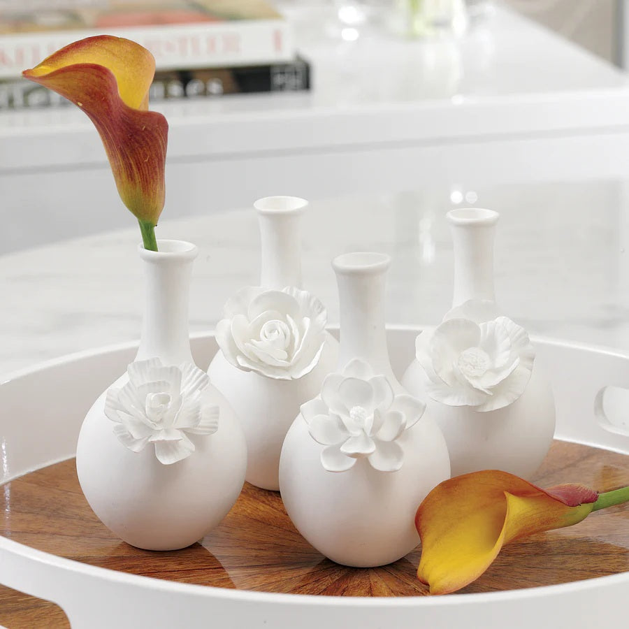 The CAMEO LONG NECK PORCELAIN BUD VASE by ZODAX is a round, white vase with a matte finish, featuring a narrow neck and a detailed floral embellishment on the front.