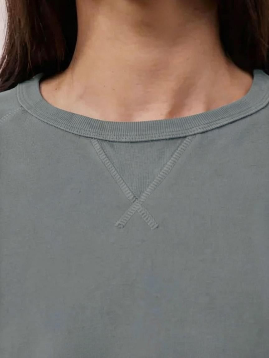 A close-up view of a person wearing the HARTFORD light fleece sweatshirt in charcoal, made in Portugal, featuring a distinctive X-shaped decorative stitch detail at the base of the collar.