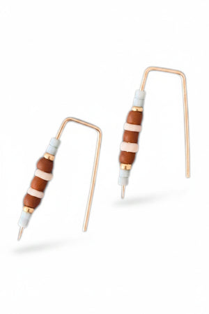 ALICE RISE - LITTLE QUILL EARRINGS IN TERRACOTTA by ALICE RISE rest on a textured gray surface, their unique design reminiscent of bent electronic resistors—perfect inspiration for handmade jewelry enthusiasts.