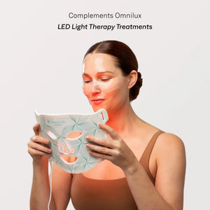 A woman removes an OMNILUX - HYDROGEL FACIAL MASK infused with Hyaluronic Acid from her face. Text above reads, “Includes 3 Hydrogel Facial Masks by OMNILUX.”.