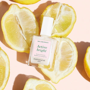 A nail polish brush and swatches appear beside text featuring the MANUCURIST - ACTIVE™ BRIGHT TREATMENT POLISH by MANUCURIST INC, emphasizing easy application, fast drying, a buildable make-up effect, and an enriched formula with active ingredients—perfect for plant-based nail care or as a brightening treatment polish.