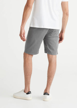 A person wearing a white t-shirt, DUER Live Free Journey Shorts in Titanium, and white sneakers stands with one hand in their pocket against a plain background.