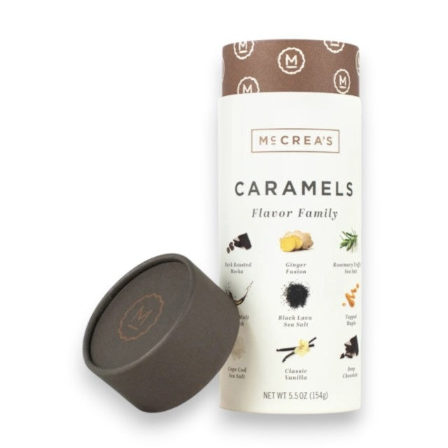 A cylindrical container labeled “McCREA’S CANDIES - FLAVOR FAMILY CARAMELS” from McCREA’S CANDIES features a brown lid—resting against the side—and charming illustrations of caramel flavors such as coffee, ginger, rosemary, sea salt, and vanilla. This collection of handcrafted caramels celebrates classic favorites and is proudly made in the USA.