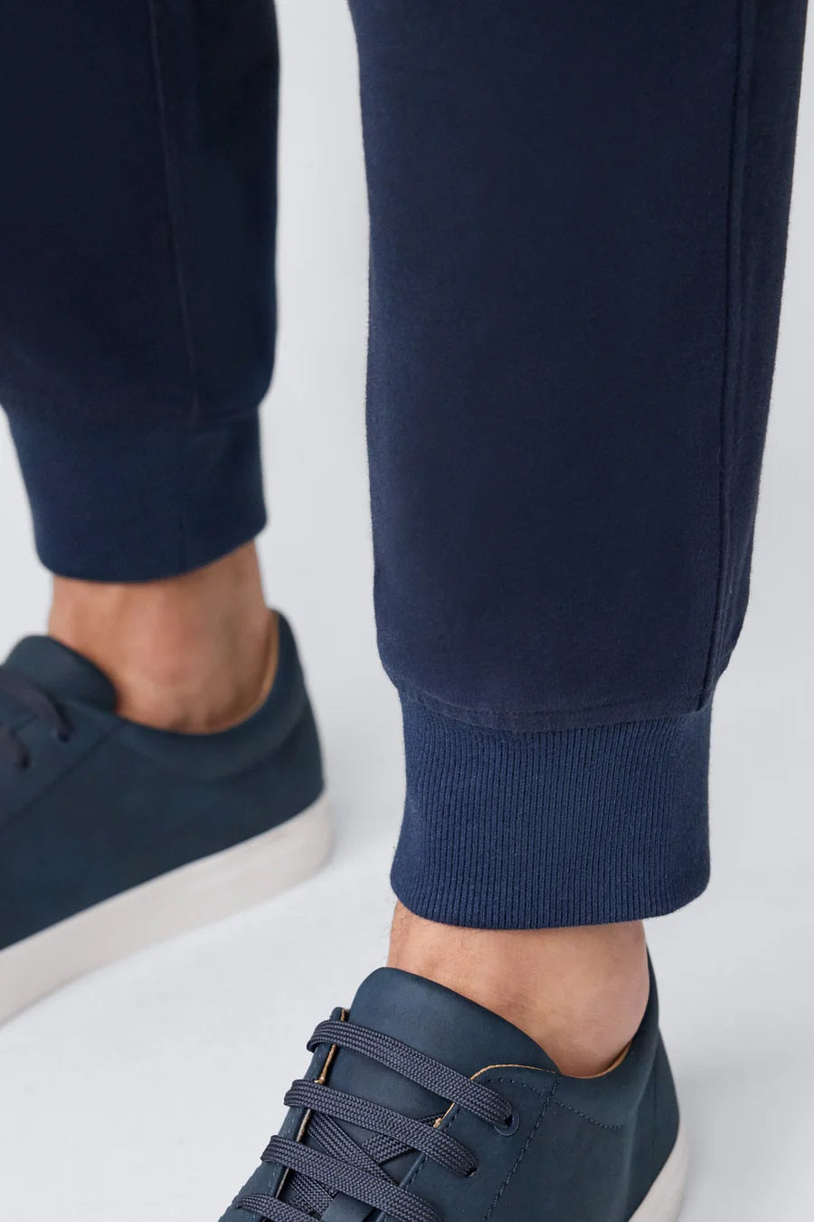 A person wears MACK WELDON ACE Relaxed Fit Sweatpants in True Navy - Bird’s Eye, styled with pockets and matching navy sneakers, against a plain light gray background. Only the lower body is visible.