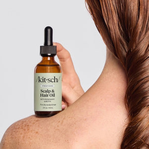 A dropper bottle and box of KITSCH - STRENGTHENING HAIR & SCALP OIL, featuring rosemary and biotin for dry scalp and hair, in a 2 fl. oz. size, are displayed against a simple light background. This plant-based formula by KITSCH is designed to support scalp health and strengthen hair.