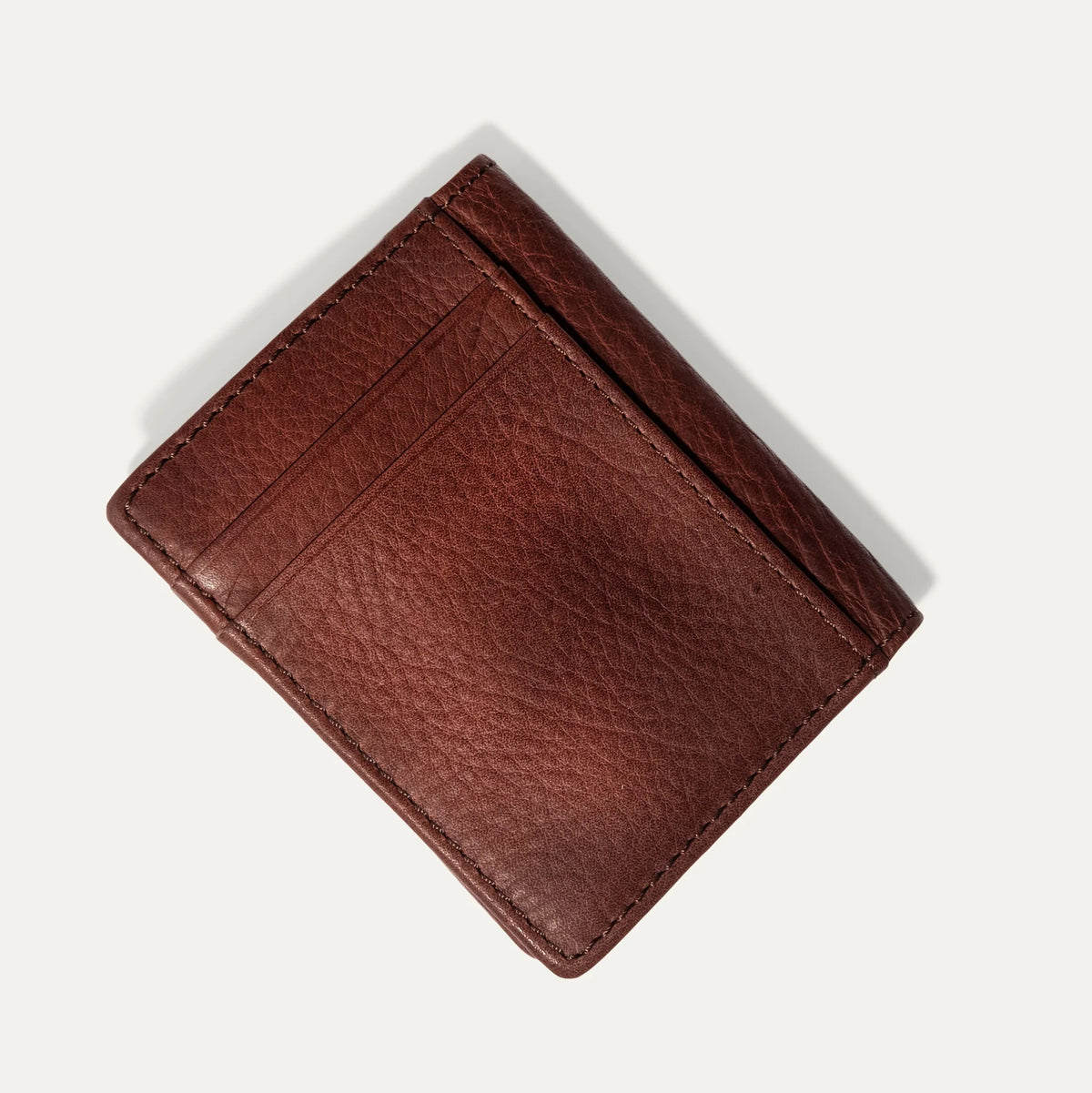 The WILL LEATHER GOODS Classic Money Clip sits atop an open full-grain leather wallet, both in brown, showcasing card slots against a plain light background.