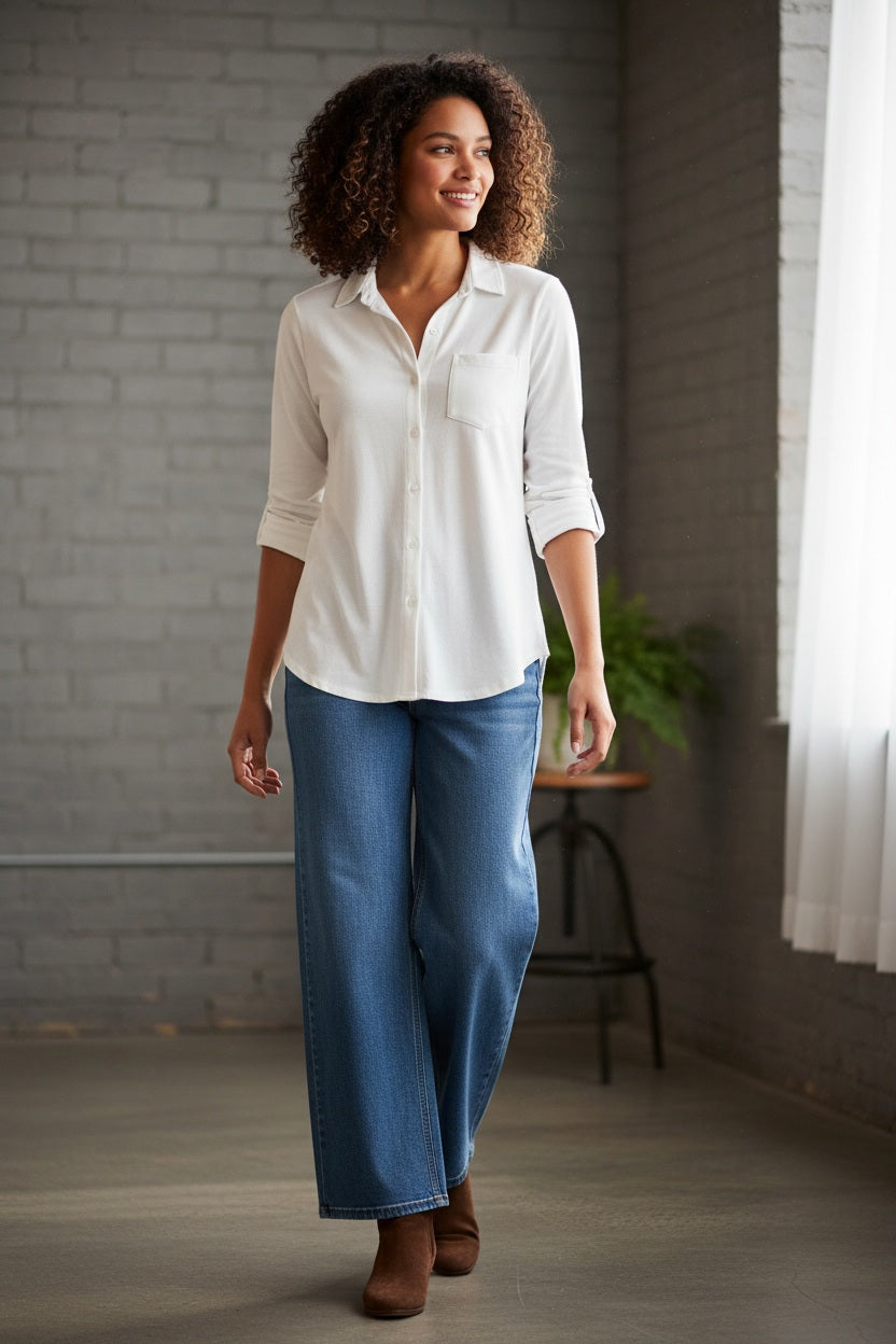 A woman with curly hair models the FRANK &amp; EILEEN WAVERLY NYC Button Up Shirt in Vintage Jersey White, shown indoors from shoulders to waist, hand on hip, highlighting its classic chest pocket.