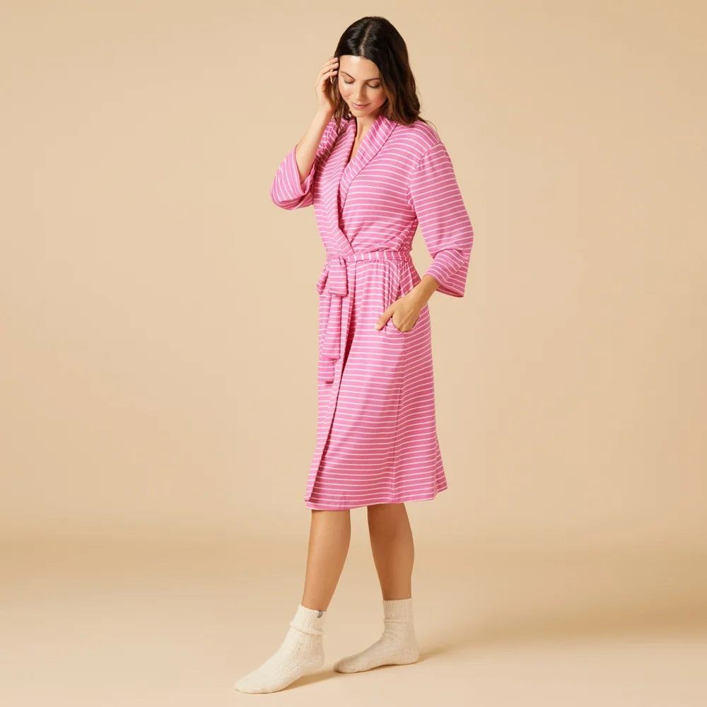 A woman wears a SOFTIES - DREAM SHAWL COLLAR ROBE IN FUSCHIA STRIPE over a matching tank top and drawstring shorts, offering spa-like luxury.