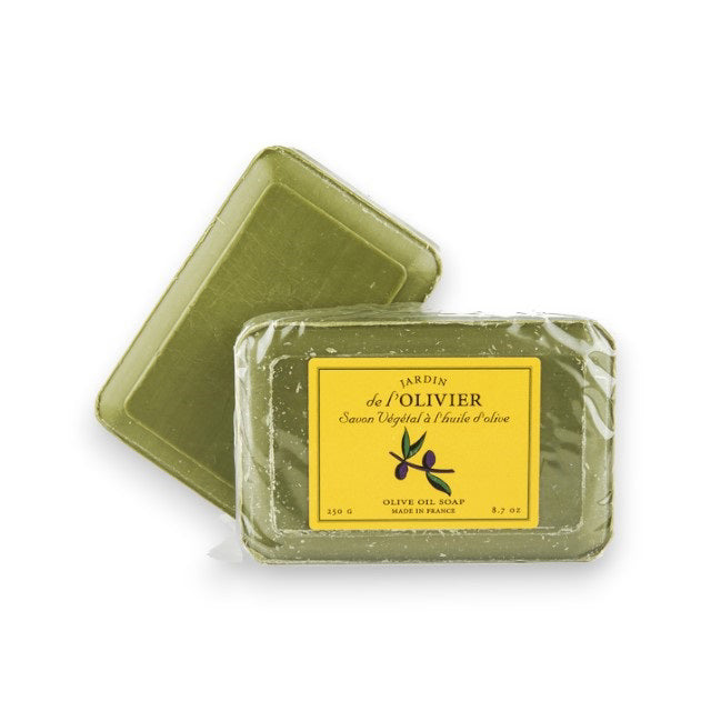 Two green bars of BAUDELAIRE - JARDIN DE L&#39;OLIVIER BATH BAR are shown. The soap in the foreground has a yellow label with black text that reads &quot;L&#39;ARDIN de l&#39;OLIVIER&quot; and &quot;OLIVE OIL SOAP MADE IN FRANCE.&quot; The soap in the background, infused with lavender, showcases its plain green surface without packaging.