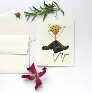 The PETAL PEOPLE PRESS - YAY CONGRATULATIONS CARD by PETAL PEOPLE PRESS features a delightful Petal Person crafted from pressed flowers and leaves, resembling a dancer. The design includes a cluster of blossoms for the head, thin stems forming raised arms, and an elegantly flaring dark skirt stemming from the leafy body. Two small buds accompany this charming figure, making it perfect for a celebration card.
